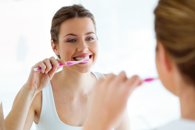 Giovane donna graziosa che pulisce i suoi denti nel bagno a casa.