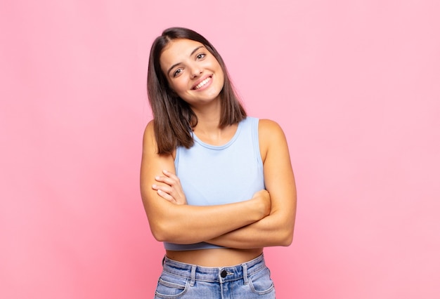 Giovane donna graziosa che ride felice con le braccia incrociate, con una posa rilassata, positiva e soddisfatta