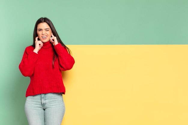 Giovane donna graziosa che sembra arrabbiata, stressata e infastidita, coprendo entrambe le orecchie con un rumore assordante, un suono o una musica ad alto volume. copia spazio per posizionare il tuo concetto