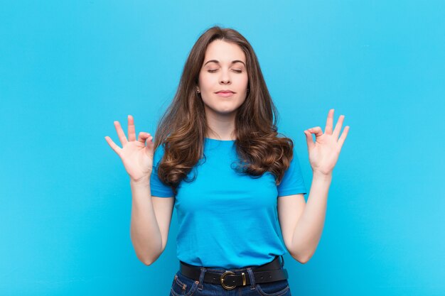 Giovane donna graziosa che sembra concentrata e meditando, sentendosi soddisfatta e rilassata, pensando o facendo una scelta sulla parete blu