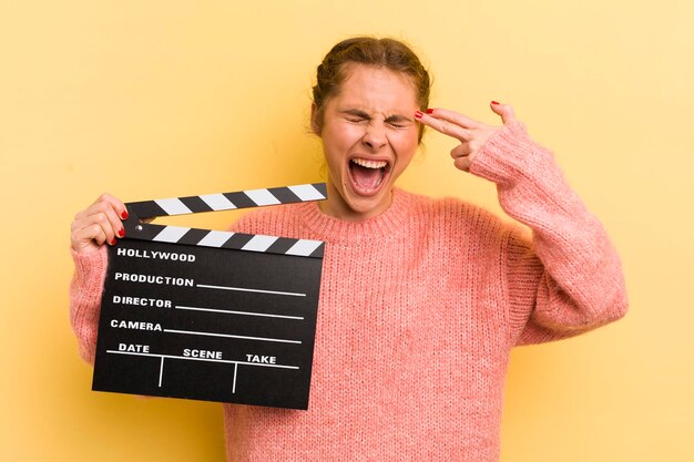 Giovane donna graziosa che sembra gesto suicida infelice e stressato facendo segno di pistola concetto di clapper cinematografico