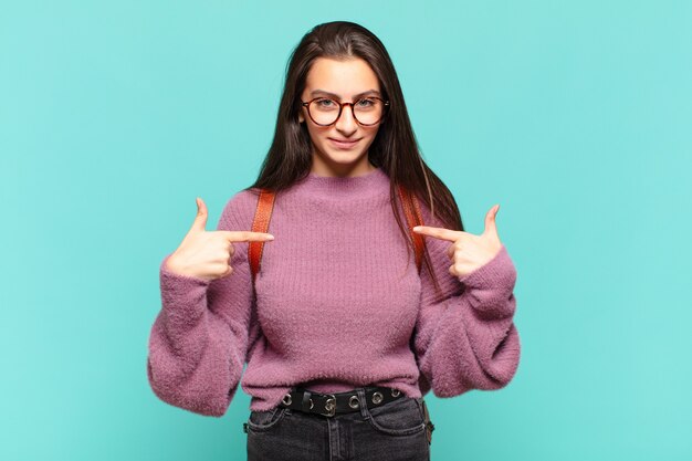 Giovane donna graziosa che sembra orgogliosa, positiva e casual che indica il petto con entrambe le mani.