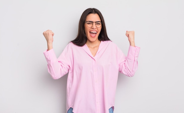 Giovane donna graziosa che si sente felice, sorpresa e orgogliosa, gridando e celebrando il successo con un grande sorriso