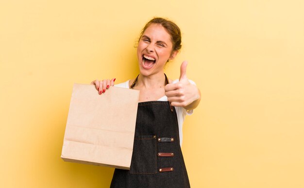 Giovane donna graziosa che si sente orgogliosa di sorridere positivamente con i pollici in su concetto di corriere fast food