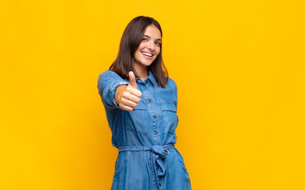 Giovane donna graziosa che si sente orgogliosa, spensierata, sicura e felice, sorridendo positivamente con i pollici in su