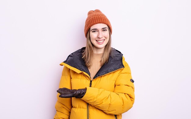 Giovane donna graziosa che sorride allegramente sentendosi felice e mostrando un concetto di inverno concetto