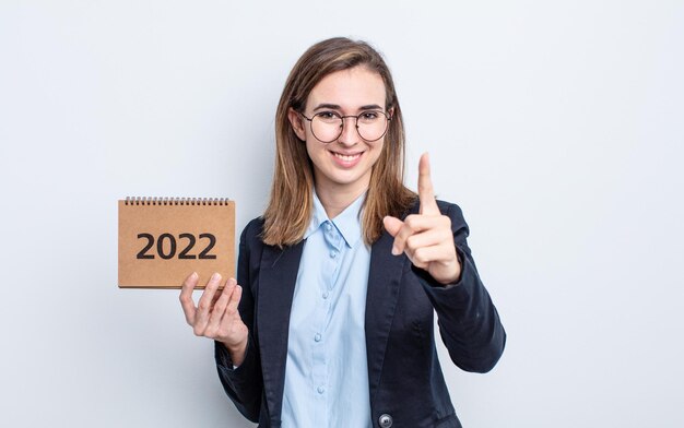 Giovane donna graziosa che sorride con orgoglio e sicurezza facendo il concetto di calendario numero uno