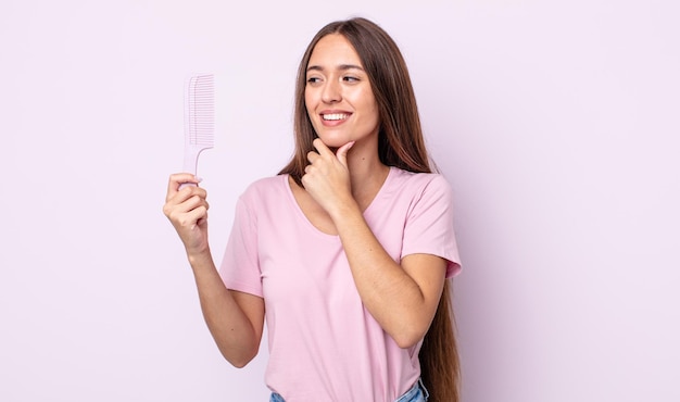 Giovane donna graziosa che sorride con un'espressione felice e sicura con la mano sul mento. concetto di pettine per capelli