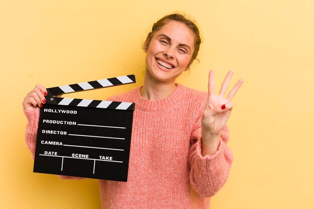 Giovane donna graziosa che sorride e che sembra amichevole che mostra il concetto del clapper del cinema numero tre