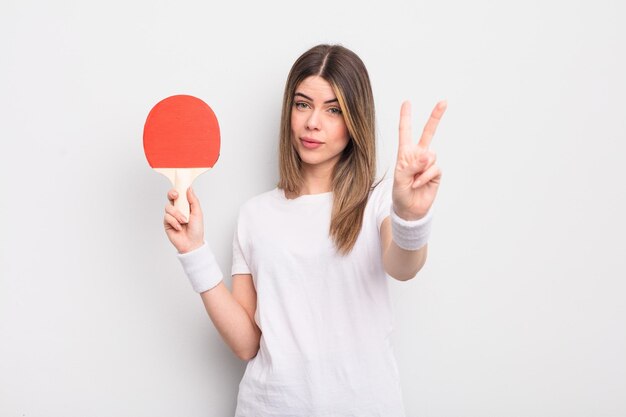 Giovane donna graziosa che sorride e che sembra amichevole che mostra il concetto di ping pong numero due