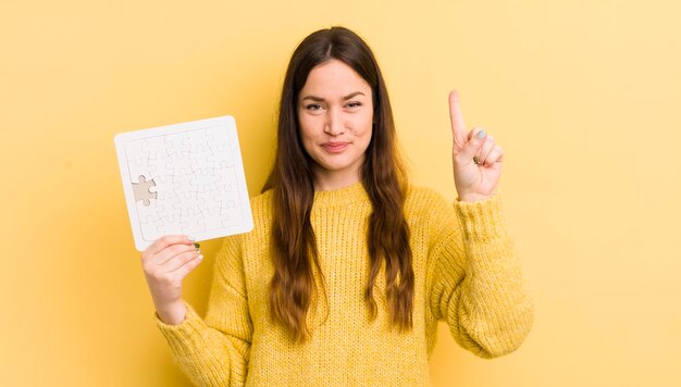 Giovane donna graziosa che sorride e che sembra amichevole mostrando il concetto di puzzle numero uno