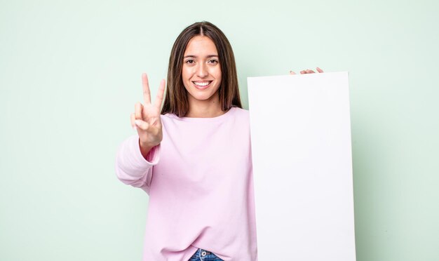 Giovane donna graziosa che sorride e che sembra amichevole, mostrando il numero due. concetto di tela vuota