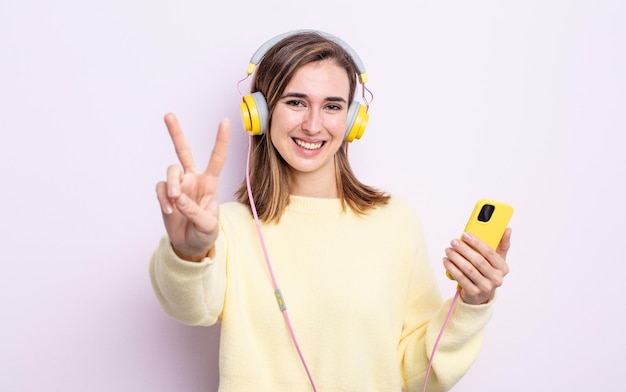 Giovane donna graziosa che sorride e sembra felice, gesturing vittoria o pace. concetto di cuffie e telefono