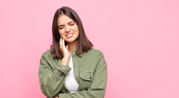 Giovane donna graziosa che tiene la guancia e soffre di mal di denti doloroso, sensazione di malessere, miserabile e infelice, alla ricerca di un dentista