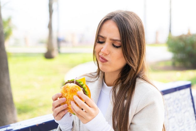 Giovane donna graziosa che tiene un hamburger all'aperto