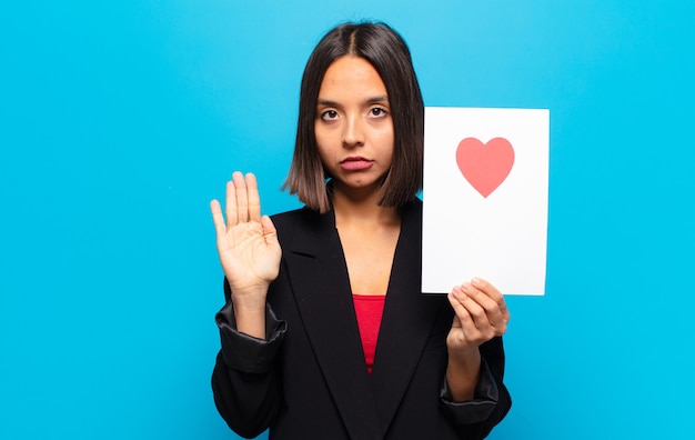 Giovane donna graziosa che tiene una carta del cuore