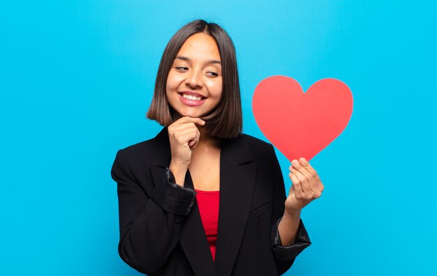 Giovane donna graziosa che tiene una carta del cuore