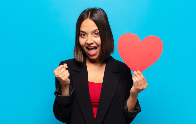 Giovane donna graziosa che tiene una carta del cuore