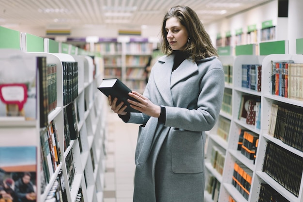 Giovane donna graziosa che trova libro in libreria