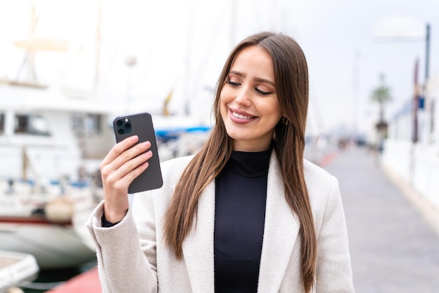 Giovane donna graziosa che utilizza il telefono cellulare all'aperto con l'espressione felice