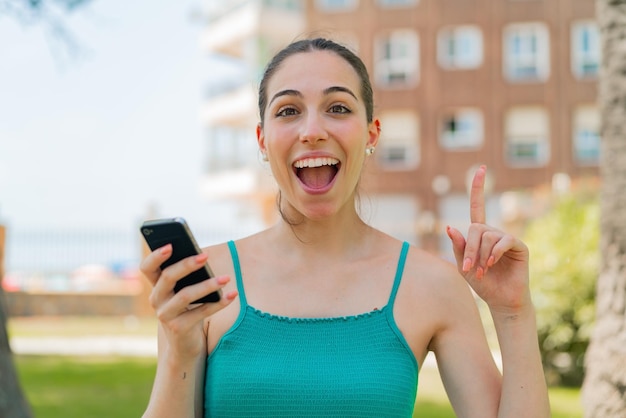 Giovane donna graziosa che utilizza il telefono cellulare all'aperto indicando una grande idea