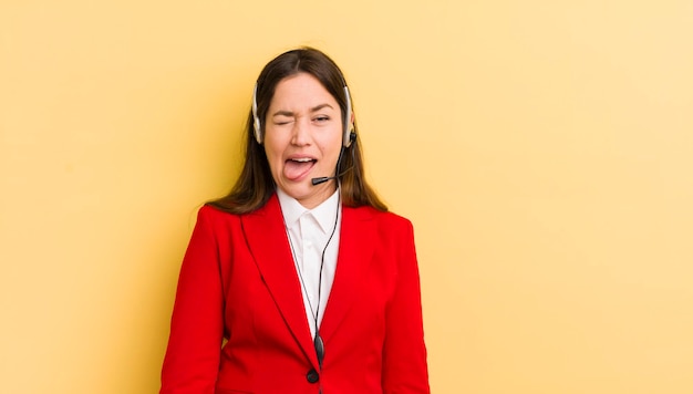 Giovane donna graziosa con atteggiamento allegro e ribelle che scherza e tira fuori la lingua concetto di telemarketing