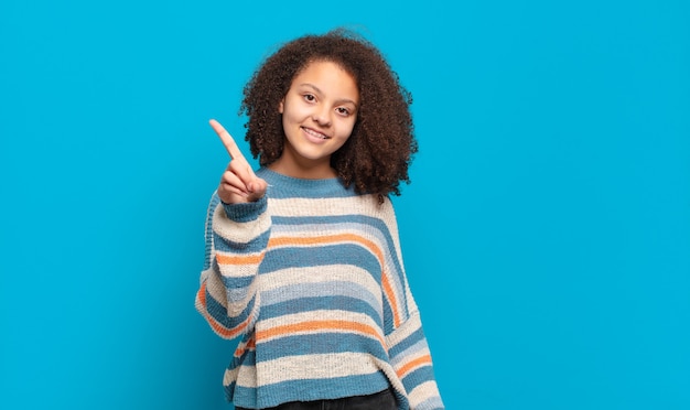 giovane donna graziosa con capelli afro e maglione a righe in posa sulla parete blu