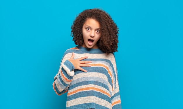 giovane donna graziosa con capelli afro e maglione a righe in posa sulla parete blu