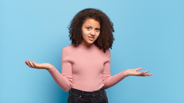 giovane donna graziosa con capelli afro e maglione rosa in posa sulla parete blu