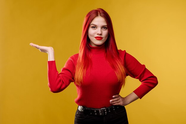 Giovane donna graziosa con capelli rossi e sweter rosso in posa su sfondo giallo