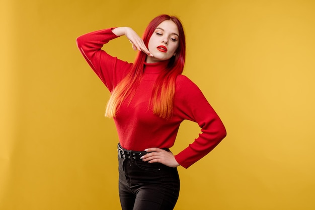 Giovane donna graziosa con capelli rossi e sweter rosso in posa su sfondo giallo