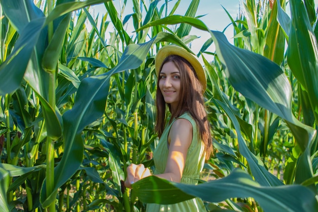 Giovane donna graziosa con il cappello giallo tra le piante di mais nel campo di mais nella stagione estiva Bereza Bielorussia