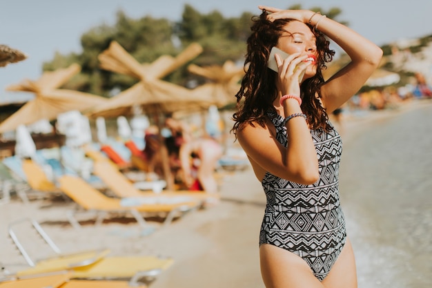 Giovane donna graziosa con il telefono cellulare sulla spiaggia