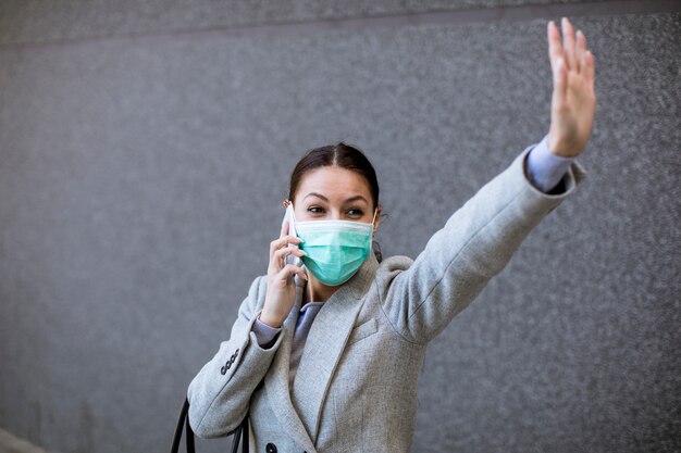 Giovane donna graziosa con la maschera facciale protettiva sulla via