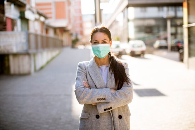 Giovane donna graziosa con la maschera facciale protettiva sulla via