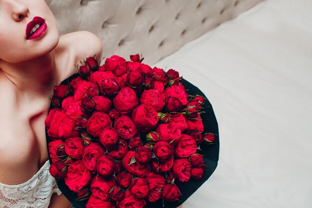 Giovane donna graziosa con le labbra e le rose rosse brillanti luminose
