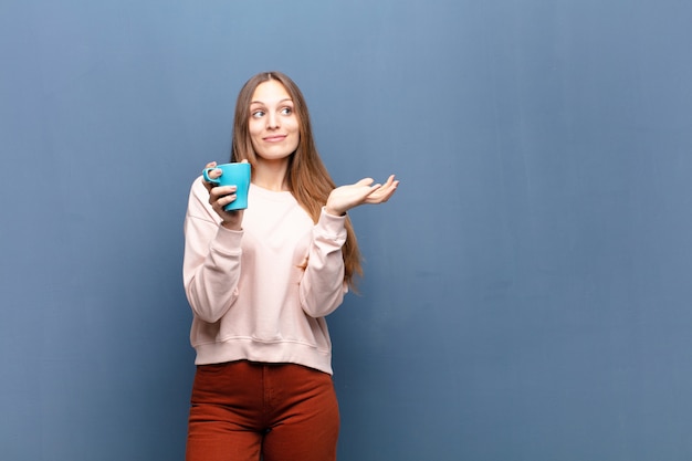 Giovane donna graziosa con un caffè contro la parete blu con un copyspace