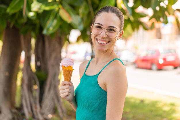 Giovane donna graziosa con un gelato alla cornetta all'aperto sorridendo molto