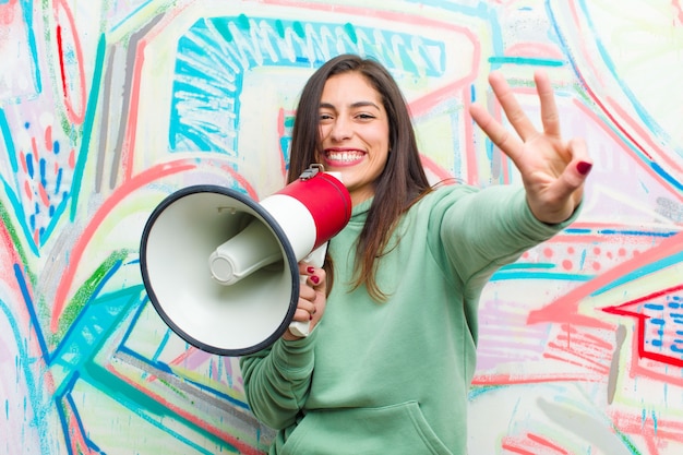 Giovane donna graziosa con un megafono contro il muro di graffiti