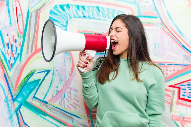 Giovane donna graziosa con un megafono contro il muro di graffiti