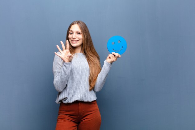 Giovane donna graziosa con una faccia sorridente contro la parete blu con uno spazio di copia