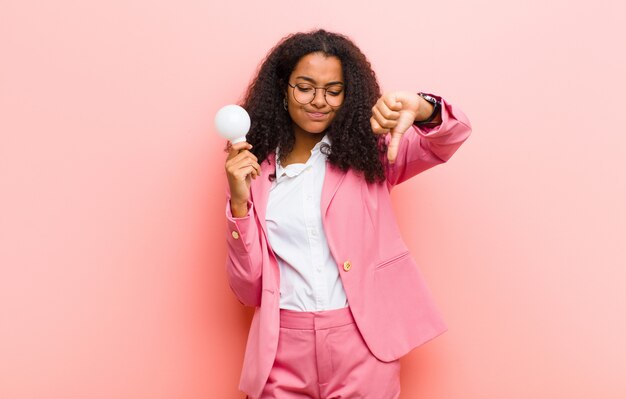 Giovane donna graziosa con una lampadina che ha un'idea contro la parete rosa