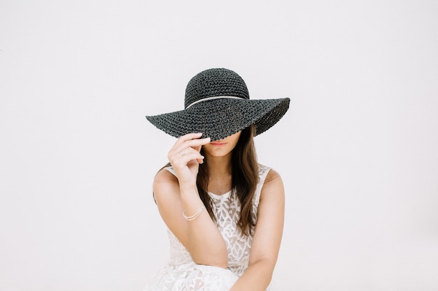 Giovane donna graziosa in abito bianco con cappello nero