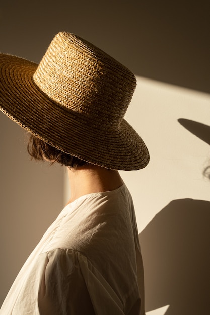 Giovane donna graziosa in cappello di paglia e prendisole vestito bianco contro il muro. Silhouette in presenza di luce solare. Ombre sul muro