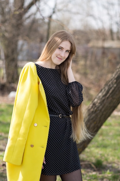 Giovane donna graziosa in cappotto giallo e vestito nero fuori