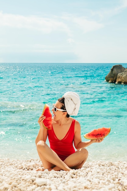 Giovane donna graziosa in costume da bagno rosso in spiaggia che tiene anguria