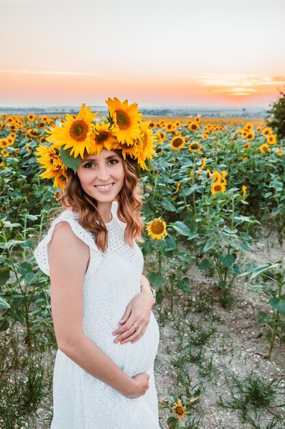 Giovane donna graziosa in prendisole bianco al campo di girasoli in fiore