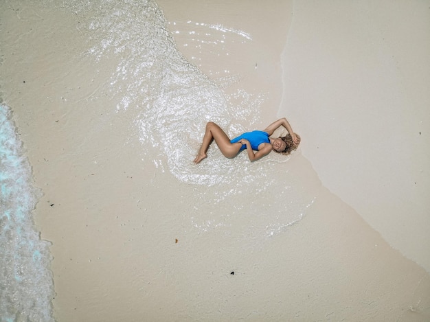 Giovane donna graziosa in un costume da bagno blu sdraiato su una spiaggia di sabbia durante la marea. Concetto di vacanza estiva