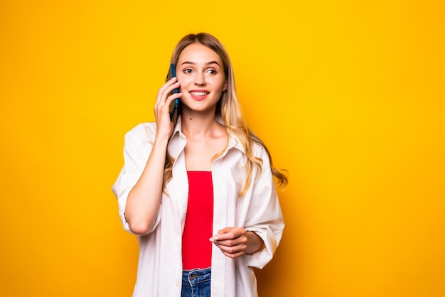 Giovane donna graziosa in vestito che parla dallo smartphone sopra la parete gialla