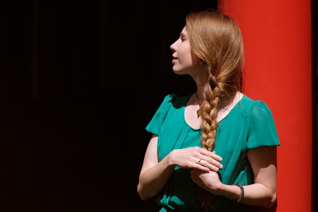 Giovane donna graziosa in vestito verde che prende il sole al sole con gli occhi chiusi, spazio della copia